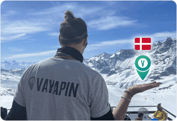 A man wearing a VayaPin t-shirt looks out over a vast, snow-covered mountain range in Switzerland